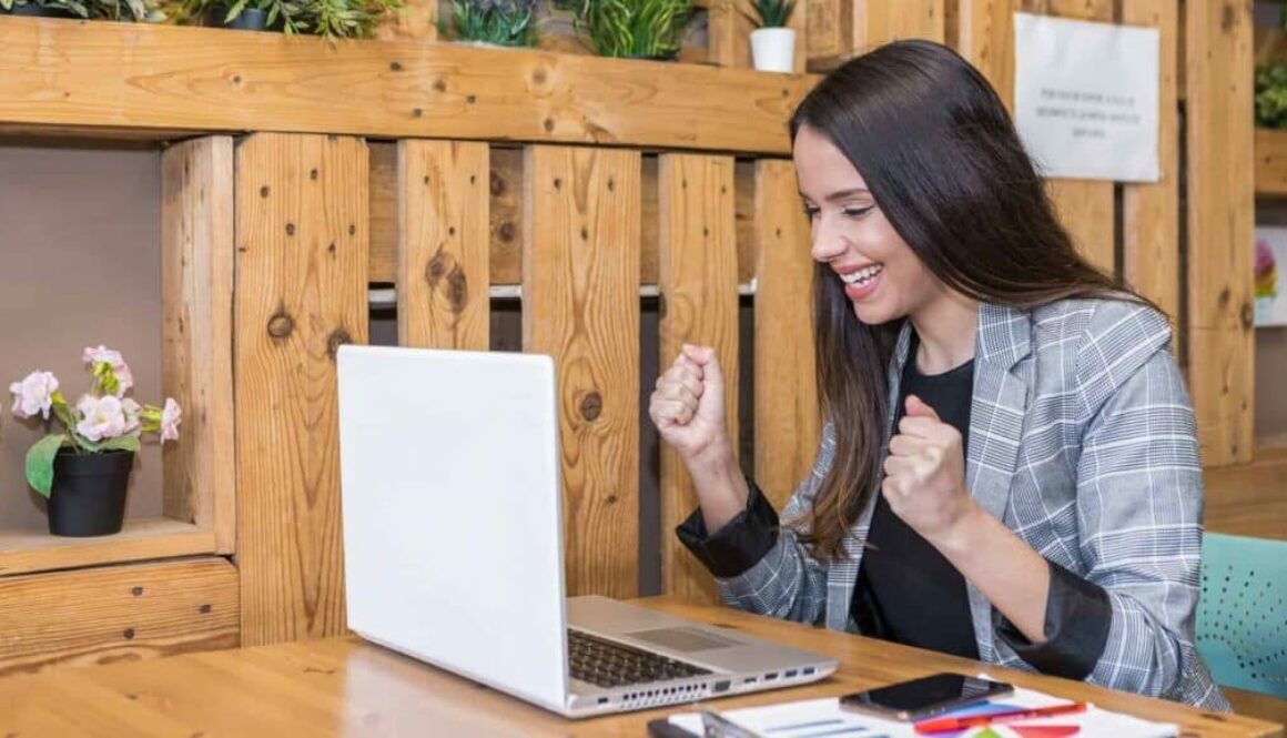 Excited woman clenching fists while working on laptop